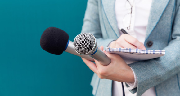 Reporterin hält zwei Mikrophone und schreibt auf einen Block