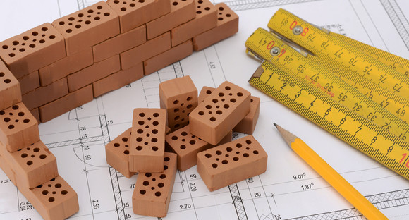 Ziegelsteine, Stift und Meterstab auf einem Bauplan