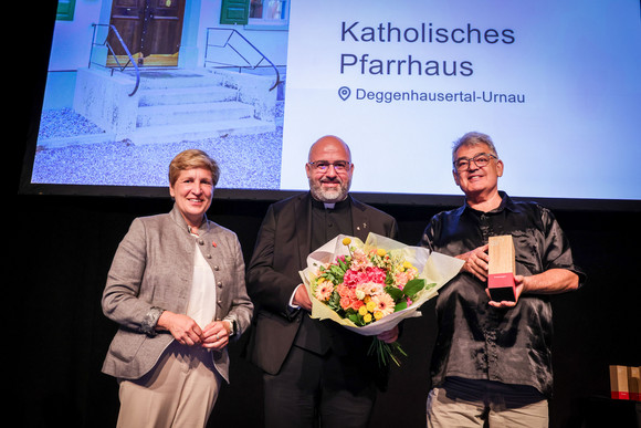 Denkmalpflege Verleihung Innovationspreis „Denkmal – Energie – Zukunft“ Ministerin Nicole Razavi MdL (links) überreicht den Innovationspreis für die Sanierung Katholischen Pfarrhauses in Deggenhausertal-Urnau an Pfarrer Jürgen Schmidt (Mitte).