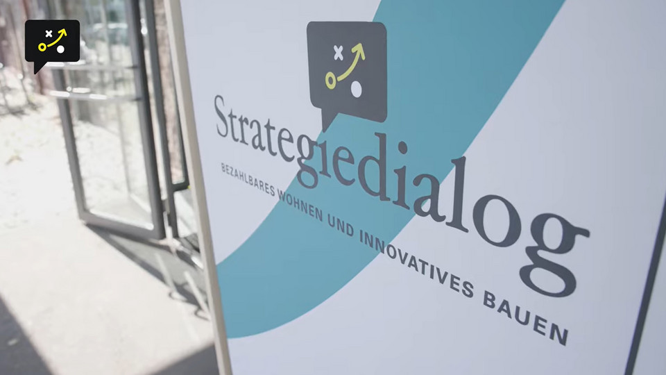 Beachflag mit Logo des Strategiedialogs Bezahlbares Wohnen und innovatives Bauen vor dem Eingang zur Jahresveranstaltung 2023 (Screenshot aus dem Video)