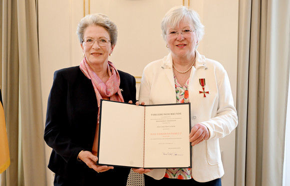 Auszeichnung Bundesverdienstkreuz für Edeltraut Stiedl Zwei ältere Frauen, beide halten eine Mappe mit einer Urkunde, die andere trägt eine Auszeichnung am Revers.