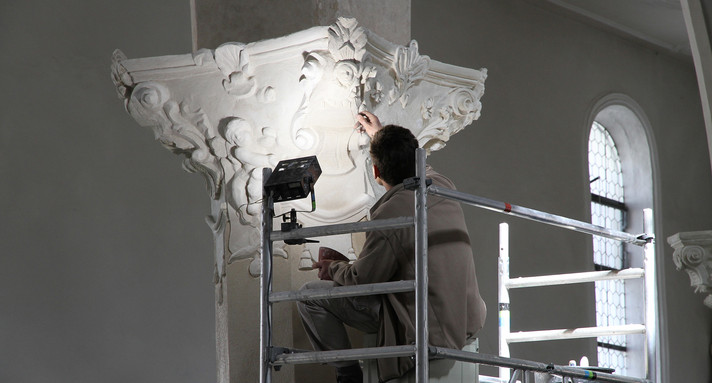 Beschreibung vom Bild: Man sieht eine Säule in einer Kirche. Ein Mann repariert die Säule.