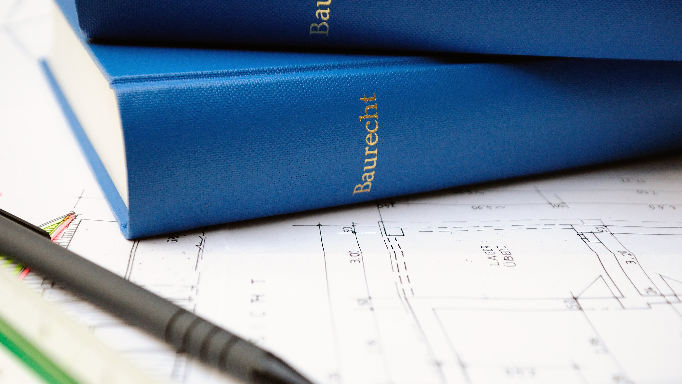 Zwei blaue Bücher über Baurecht auf Bauplan liegend neben Stift und Lineal