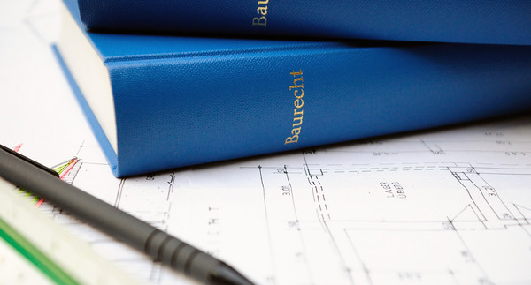 Zwei blaue Bücher über Baurecht auf Bauplan liegend neben Stift und Lineal