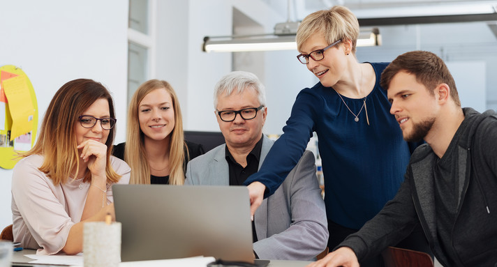 Frauen und Männer am Arbeitsplatz, eine Kollegin erklärt den anderen etwas am Laptop