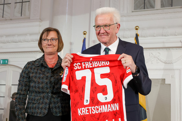 Festakt 75. Geburtstag von Ministerpräsident Winfried Kretschmann Die ehemalige Finanzministerin Edith Sitzmann (links) überreicht Ministerpräsident Winfried Kretschmann (rechts) ein Trikot des SC Freiburg mit der Nummer 75, der Aufschrift "KRETSCHMANN" sowie Unterschriften der gesamten Mannschaft..".