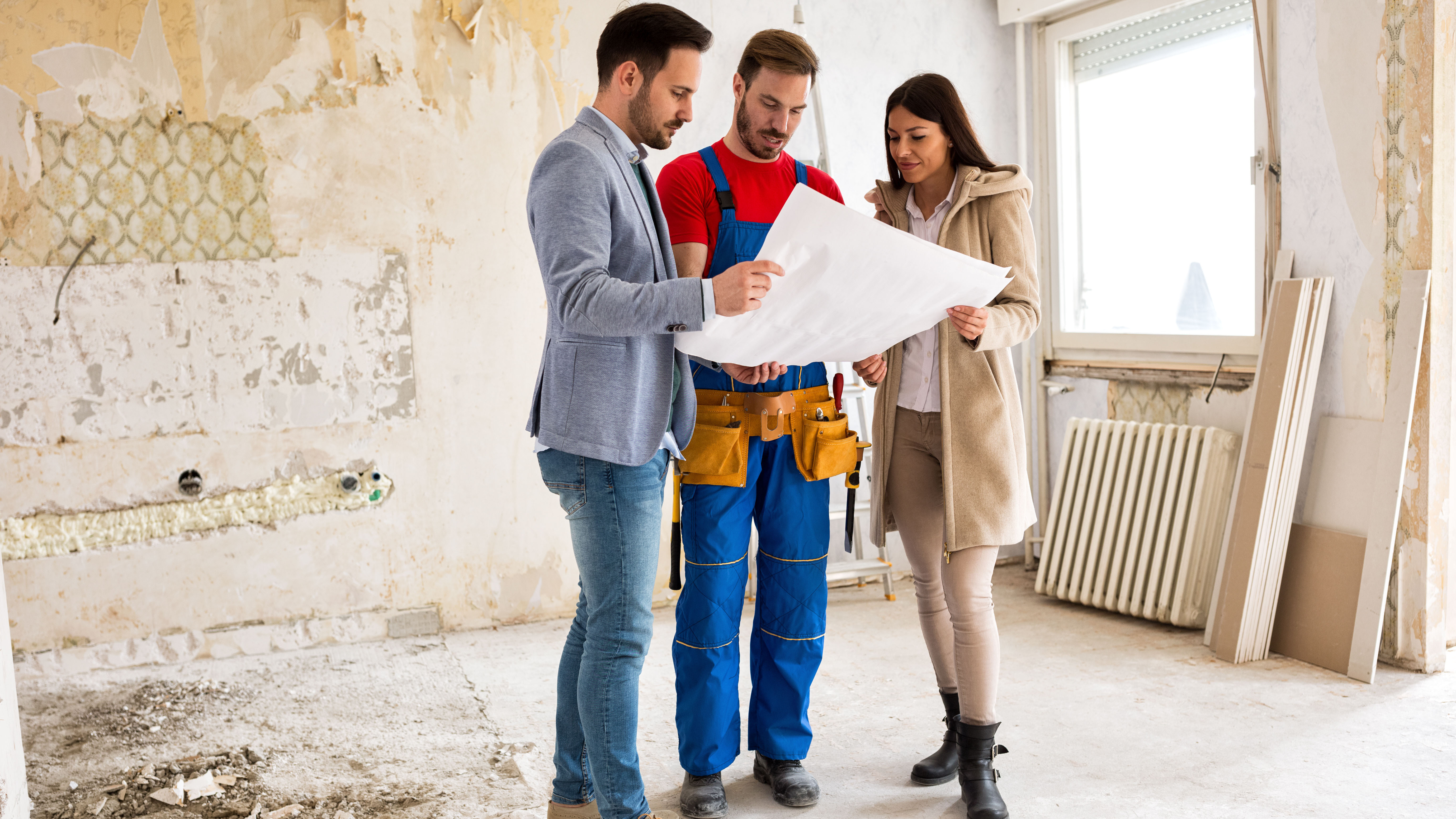 Junges Paar schaut mit dem Handwerker auf Baupläne ihrer Wohnung