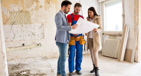 Junges Paar schaut mit dem Handwerker auf Baupläne ihrer Wohnung