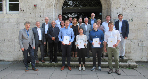 Matthias Fritz, Pia Wackler, Hannes Plott und Timo Nopper (mit Zeugnissen) nach ihrem erfolgreichen Abschluss der Staatsprüfung für den höheren vermessungstechnischen Verwaltungsdienst, zusammen mit den Mitgliedern des Prüfungsausschusses.