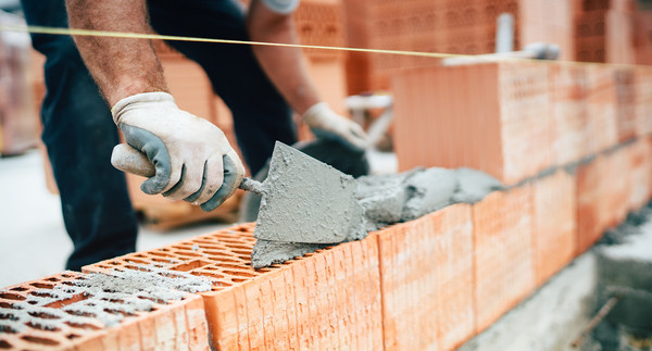 Bauarbeiter verteilt Mörtel mit einer Maurerkelle auf Ziegelsteinen, um eine Wand zu bauen