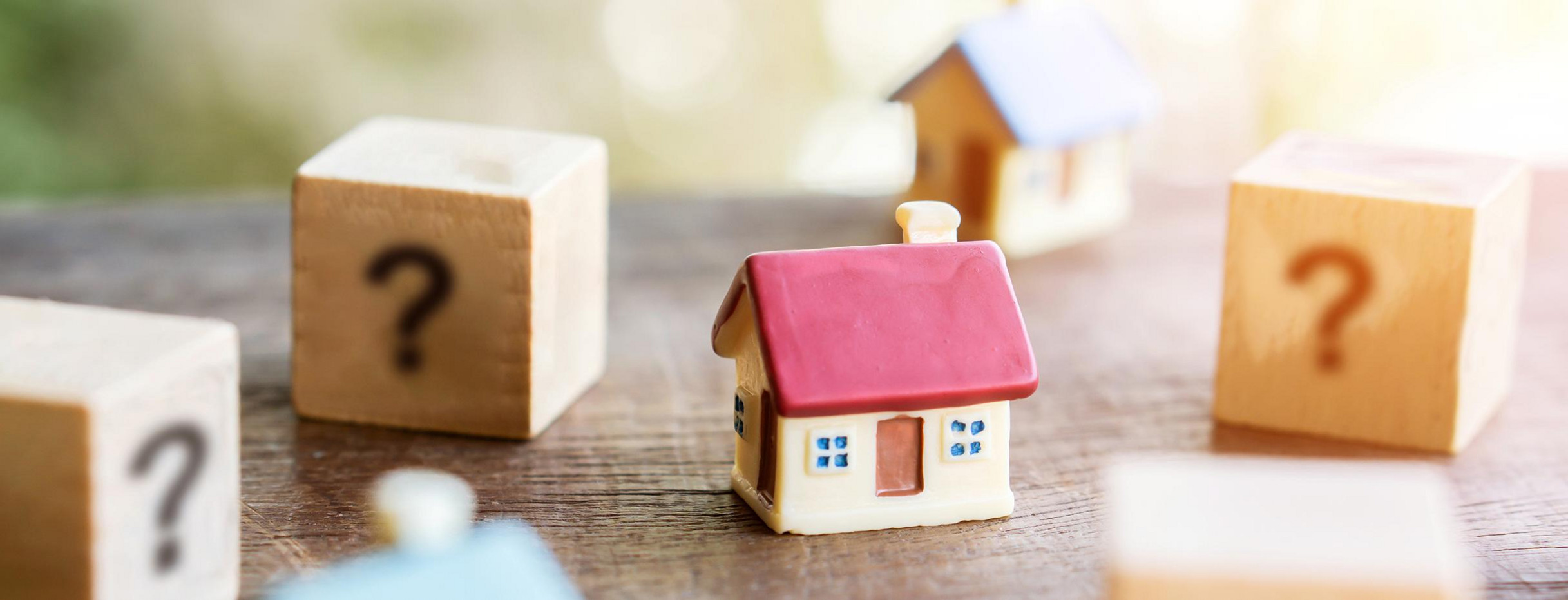 Mehrere Würfel mit Fragezeichen und Miniaturhaus als Modell zur Immobiliensuche