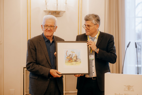 Landrat Dr. Martin Kistler (rechts), Vorsitzender des Dachverbandes der Dialekte Baden-Württemberg, übergibt Ministerpräsident Winfried Kretschmann (links) eine Zeichnung mit Äffle und Pferdle.