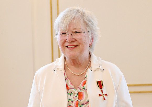 Auszeichnung Bundesverdienstkreuz für Edeltraut Stiedl Ältere Frau mit weißem Haar, Brille und Perlenkette, trägt eine weiße Jacke mit einem Orden am Revers, und lächelt.