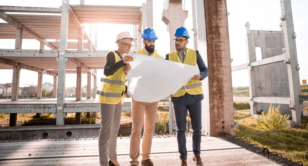Eine Prüfingenieurin und zwei Prüfingenieure begutachten einen Plan auf einer Baustelle