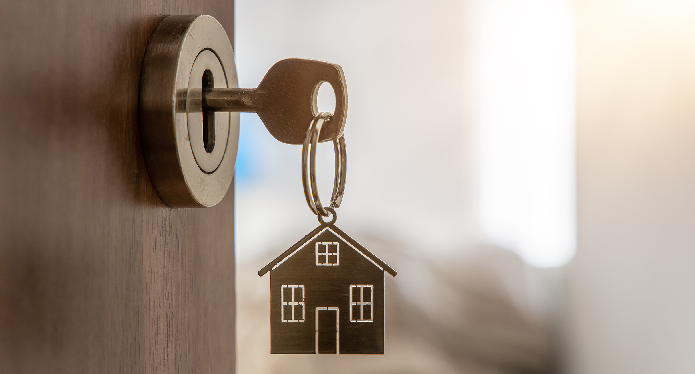 Schlüssel mit Hausminiatur-Anhänger an einer neuen Wohnungstür']